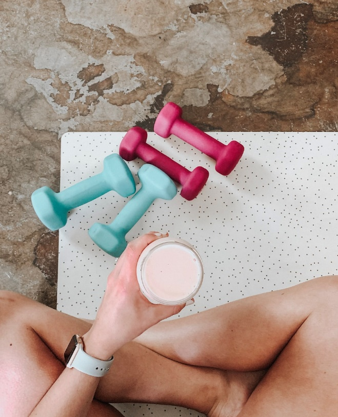 A woman holding a cup while sitting next to dumbbells